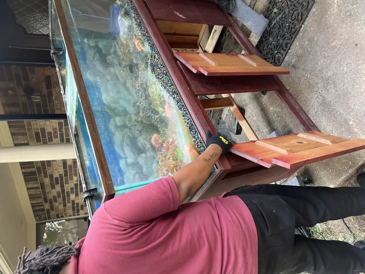 Crew member carrying a large glass aquarium out of a home in Panorama Village Conroe TX